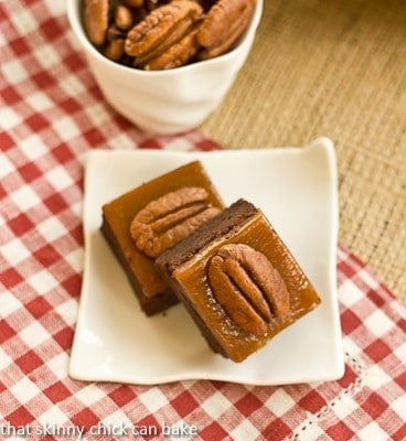 Two turtle brownies on a square white plate on a red and white checked napkin