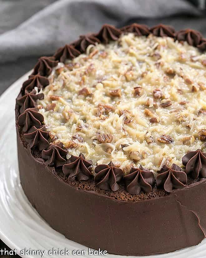 Homemade German Chocolate Cake - 4 layers of chocolate cake filled with a caramel coconut pecan filling, then iced with a rich, chocolate frosting! Perfect cake for any celebration! German Chocolate Cake on a white cake plate.
