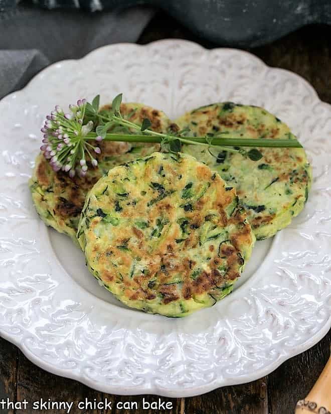 Overhead view of 3 zucchini fritter on a fancy, decorative white plate.
