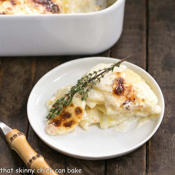 French Potato Gratin - A exquisite creamy cheesy potato casserole kissed with garlic, thyme and topped with Gruyere cheese! French Potato Gratin on a round white plate with a bamboo handled fork.