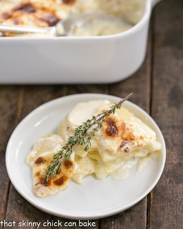 French Potato Gratin - A exquisite creamy cheesy potato casserole kissed with garlic, thyme and topped with Gruyere cheese! French Potato Gratin on a small white plate with a sprig of thyme.