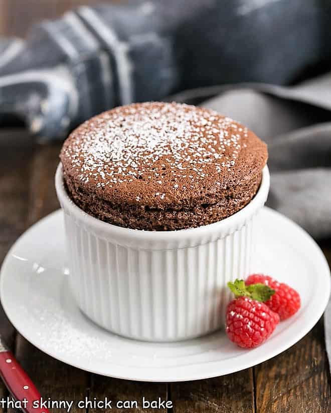 Individual Individual Chocolate Soufflés in white ramekins with a fresh raspberry garnish.