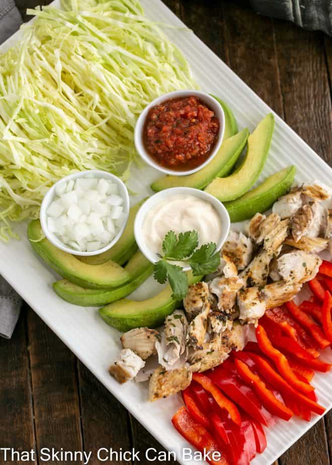 Overhead view of fish tacos with cabbage ingredients on a white ceramic platter.