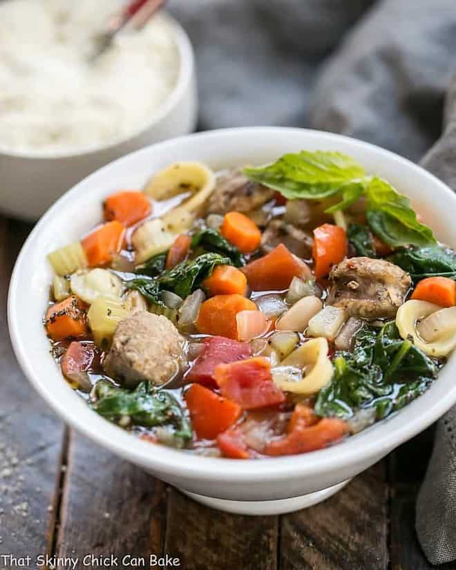 Italian Sausage and Pasta Soup in a white soup bowl in front of a bowl of Parmesan cheese.