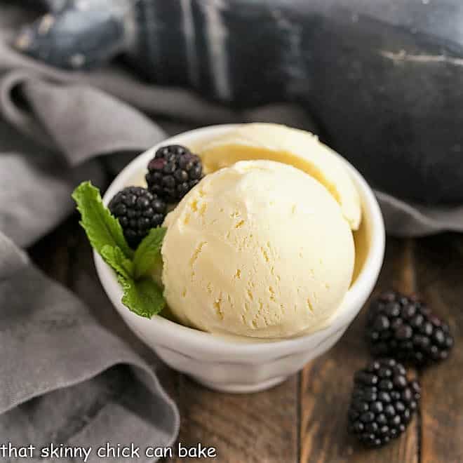 Dreamy White Chocolate Ice Cream -A rich, luscious ice cream enhanced with melted white chocolate! White Chocolate Ice Cream scoops in a white ceramic bowl with berries and mint.