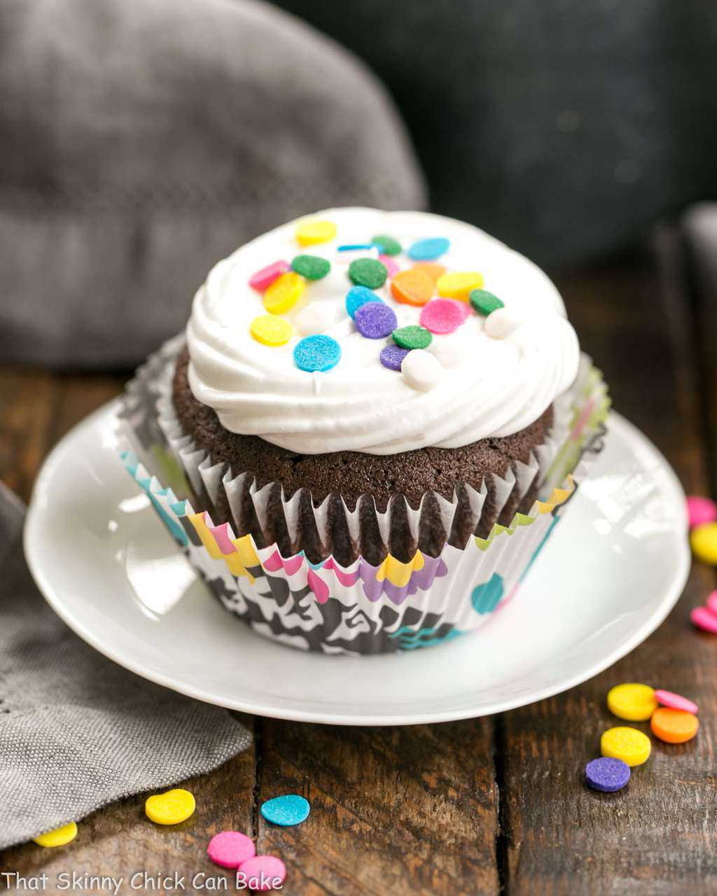 Cocoa Cupcakes with Ganache Filling - a delectable chocolate cupcake with a chocolate surprise in the middle! Cocoa Cupcakes with Ganache Filling on a small white plate topped with sprinkles.