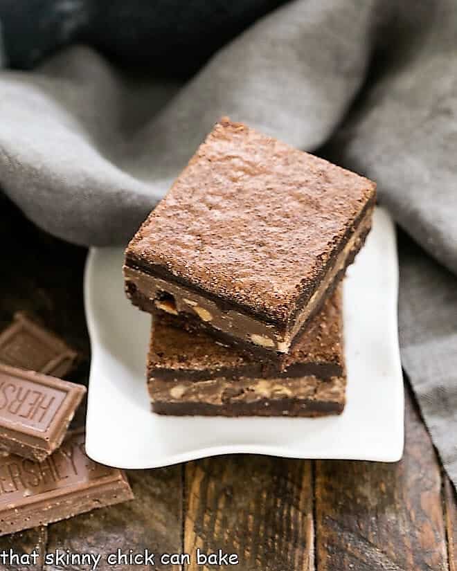 Symphony Toffee Brownies - rich, fudgy brownies with a milk chocolate, almond, toffee filling that pushes these over the top!!! Two Symphony Toffee Brownies stacked on a square white dish.