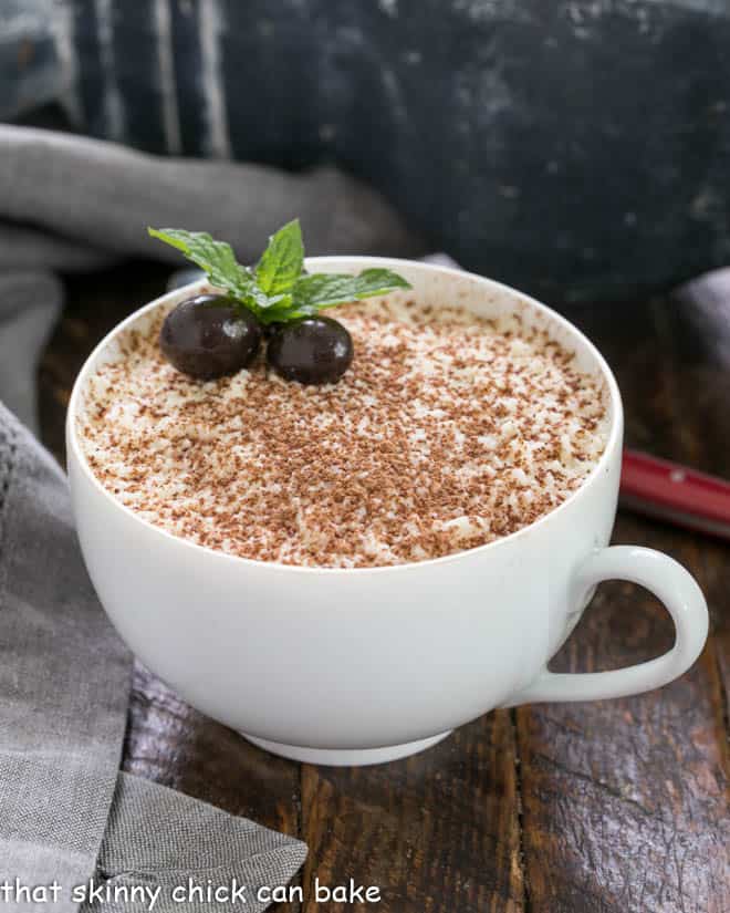 A teacup filled with chocolate tiramisu garnished with cocoa and espresso beans and a sprig of mint.