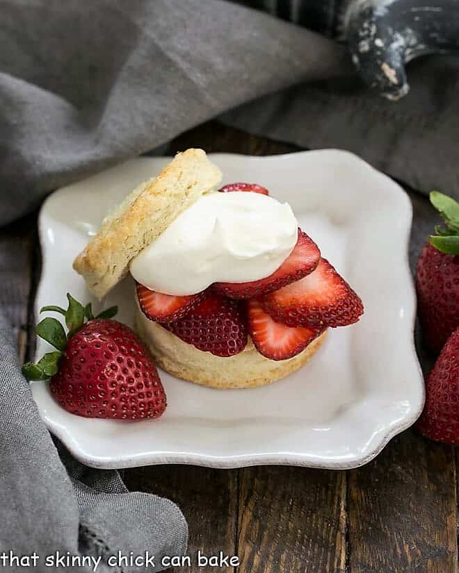 Classic Strawberry Shortcake - tender flaky biscuits topped with sweet, juicy berries and freshly whipped cream for a magnificent spring or summer dessert Classic Strawberry Shortcakes on a square white plate with a half strawberry garnish.