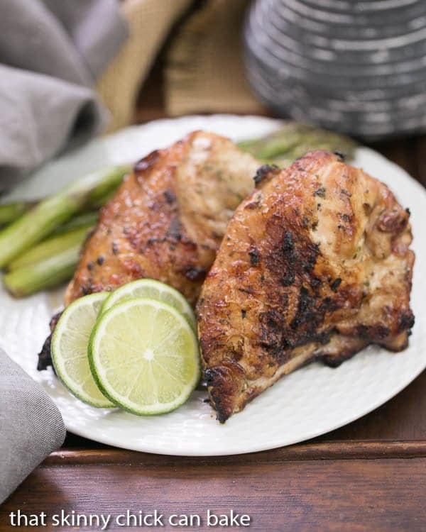 Grilled Thai Chicken - Marinated in coconut milk with fish sauce, lime juice, garlic and cilantro, this is one of the BEST grilled chicken dishes you'll ever taste! Grilled Thai Chicken on a white plate with lime slices.