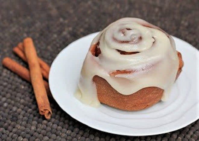 Sweet, tender classic cinnamon rolls - dripping with icing, these cinnamon buns will start your morning on a delicious note! Frosted Classic Cinnamon Roll on a white plate