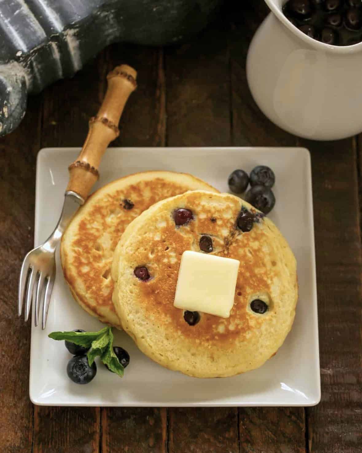 2 Blueberry Buttermilk Pancakes on a square white plate with a bamboo handle fork.