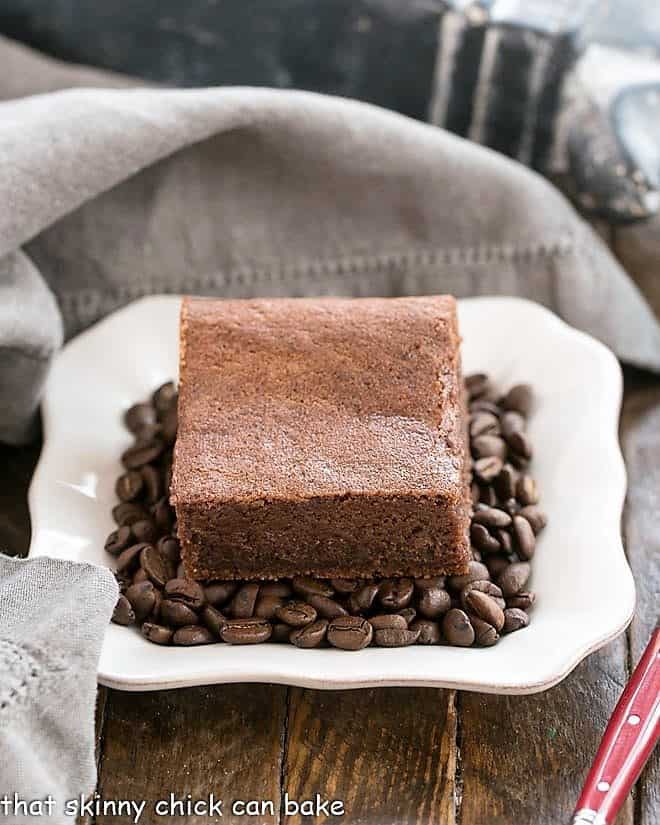 These Fudgy Kahlua Brownies - rich, dense, even a bit gooey. Brownie perfection in every bite! Kahlua Brownies on a bed of coffee beans on a square white plate