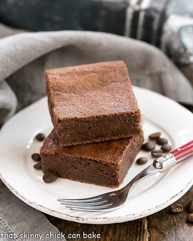 These Fudgy Kahlua Brownies - rich, dense, even a bit gooey. Brownie perfection in every bite! Kahlua Brownies on a round white plate with coffee beans and a fork.