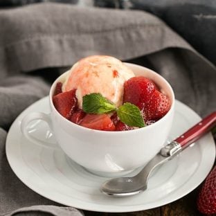 Cheesecake Ice Cream with Strawberry Sauce in a white teacup with a red handled spoon