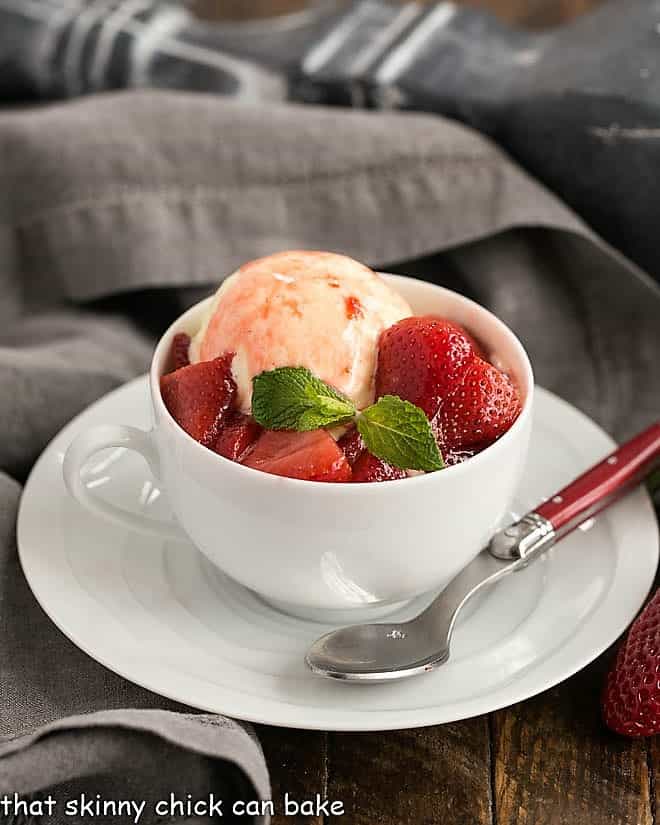 Cheesecake Ice Cream with Strawberry Sauce - rich, dreamy ice cream reminiscent of cheesecake topped with a sweet berry sauce Cheesecake Ice Cream with Strawberry Sauce in a white teacup with a red handled spoon.