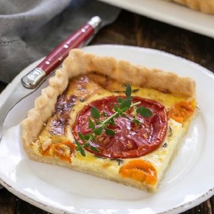 Slice of Tomato Gruyere Tart on a white plate with a red handle fork