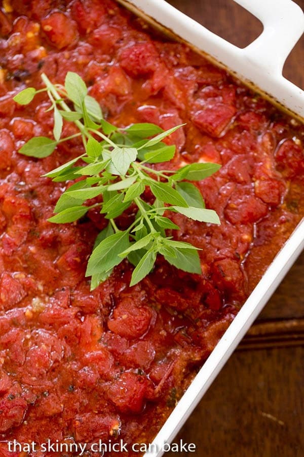 Chicken Feta Casserole - A fabulous casserole chock full of tomatoes, garlic, feta and herbs! Chicken Feta Casserole in a white casserole dish with a sprig of fresh basil.