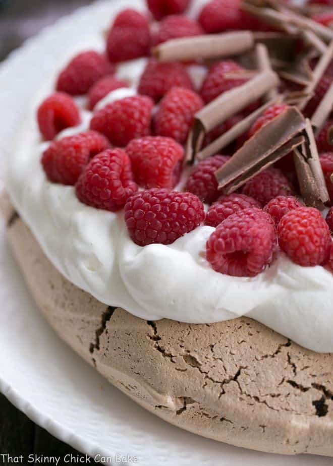 Chocolate Raspberry Pavlova - A sublime dessert with a chocolate meringue topped with berries and cream Close view of Chocolate Raspberry Pavlova on a white serving plate.