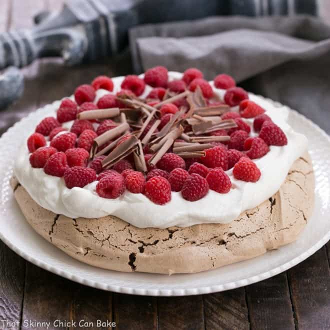 Chocolate Raspberry Pavlova - A sublime dessert with a chocolate meringue topped with berries and cream Chocolate Raspberry Pavlova on a white ceramic plate topped with cream, berries and chocolate.