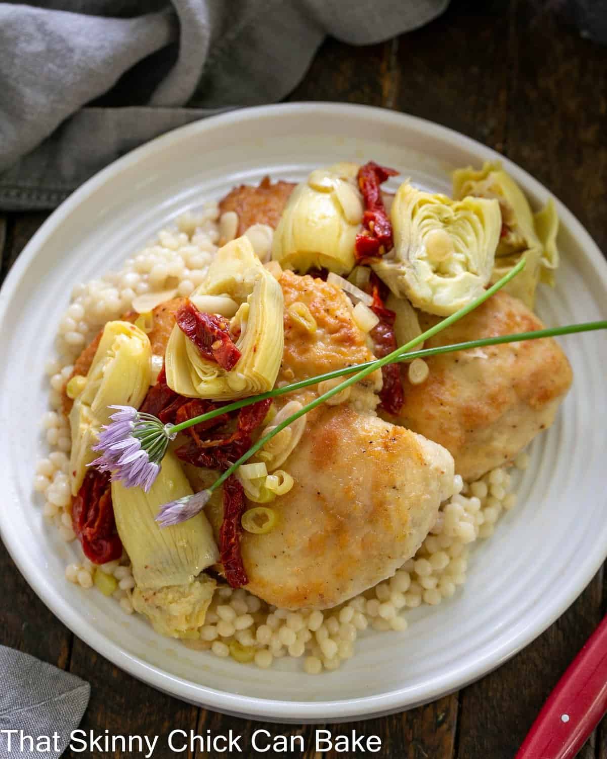 Chicken with Artichokes over Israeli Couscous - an easy, delectable entree that's quick to prepare! overhead view of chicken with artichokes on a white plate.
