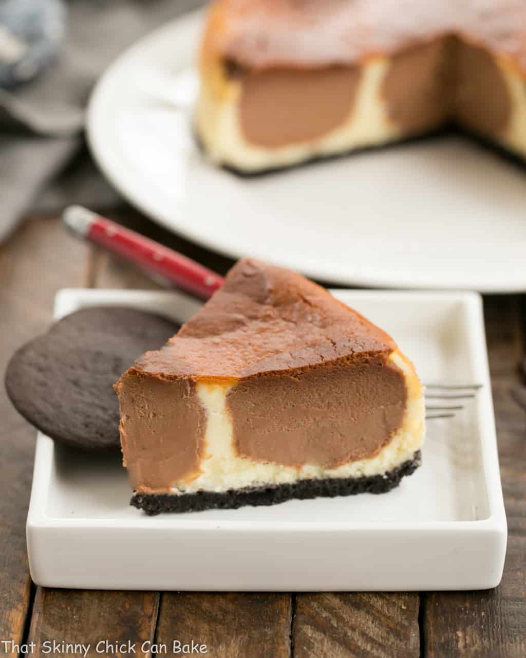 Polka Dot Cheesecake slice on a square plate with a couple chocolate wafer cookies and a red handled fork