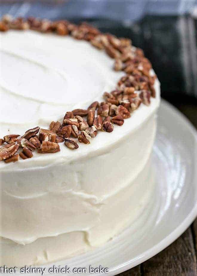 Partial view of whole cheesecake stuffed carrot cake with cream cheese frosting.