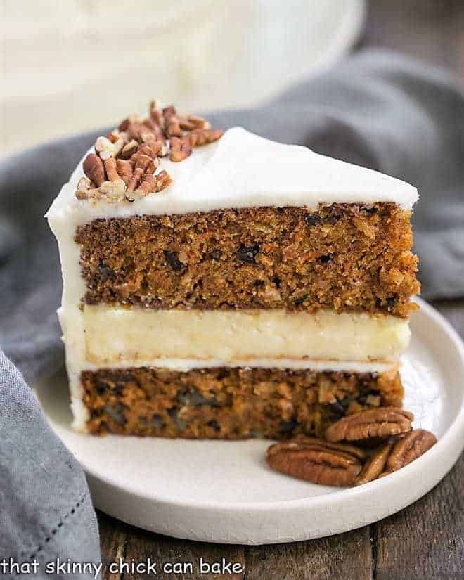 Slice of Cheesecake Filled Carrot Cake on a rimmed white plate with pecans.