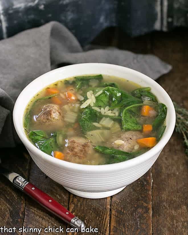 Italian Wedding Soup in a white bowl with a red handled spoon.