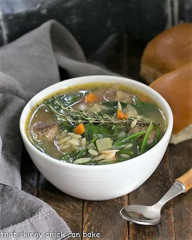 Italian wedding soup in a white soup bowl and a bamboo handled soup spoon.