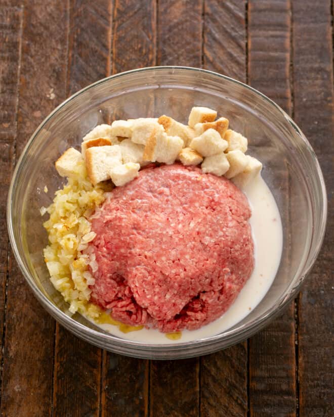 Sauteed onions, garlic, milk, bread cubes and meatloaf mix in a bowl.