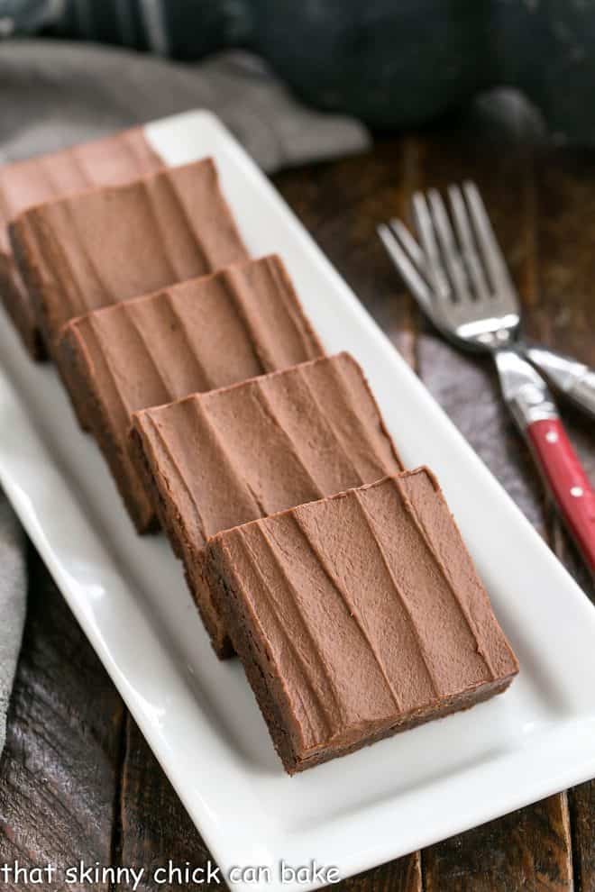 Chewy Brownies lined up on a white ceramic tray next to 2 red handle forks