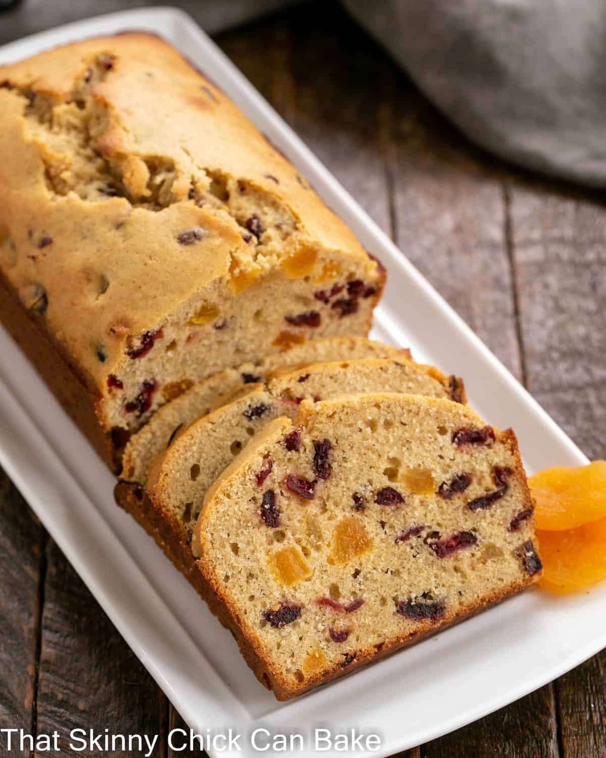 Apricot Quick Bread - a tender loaf packed full of dried fruit Apricot Quick Bread partially sliced with dried apricots to garnish on a white tray.