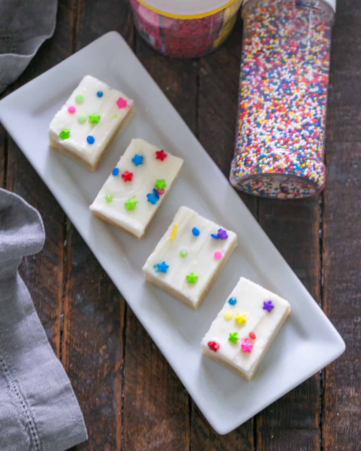 Sugar cookie bars with frosting and sprinkles on a white ceramic tray.