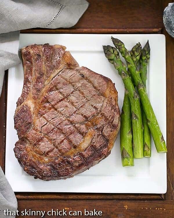 How to Grill Perfect Rib Eye Steaks - Tips for how to grill steaks at home! Rib Eye Steak on a dinner plate with asparagus.