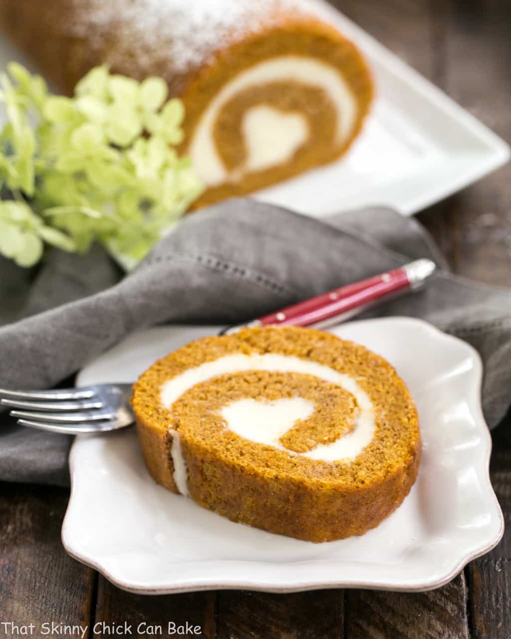 Pumpkin Cake Roll Recipe- With a cream cheese filling, this classic fall pumpkin roll always gets rave reviews! Old Fashioned Pumpkin Roll slice reveals a swirl of cream cheese filling on a white ceramic plate.