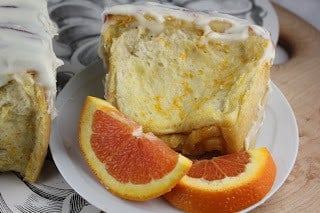 Slice of orange coffee cake on a plate with orange slices.