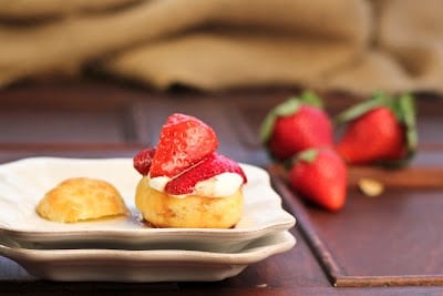 A close up of Cream puff filled with whipped cream and topped with berries on a stack of plates