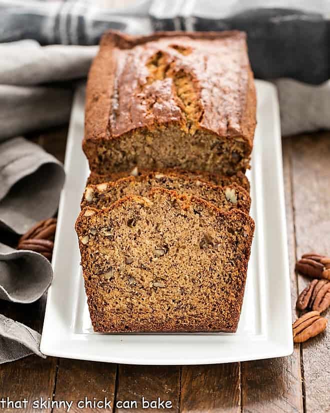 Moist Banana Bread Recipe - Perfect brunch, breakfast or snack! Always a winner! A partially sliced loaf of banana nut bread on a white platter.
