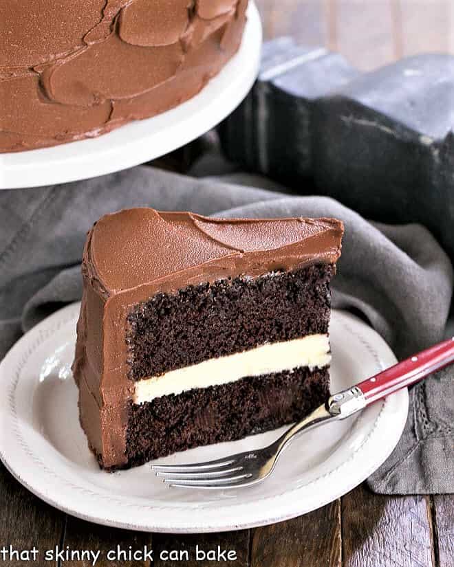 Chocolate Cake Recipe Filled with White Chocolate Ganache - a rich chocolate dessert for dark and white chocolate lovers White Chocolate Ganache slice on a dessert plate with a red handled fork.