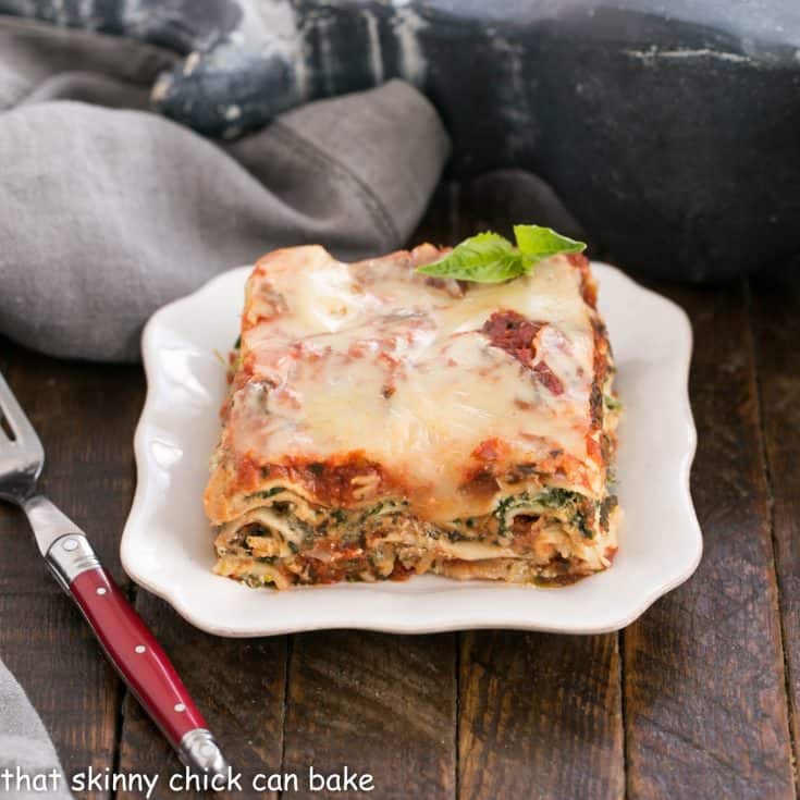 A slice of spinach lasagna on a white plate with a red handled fork