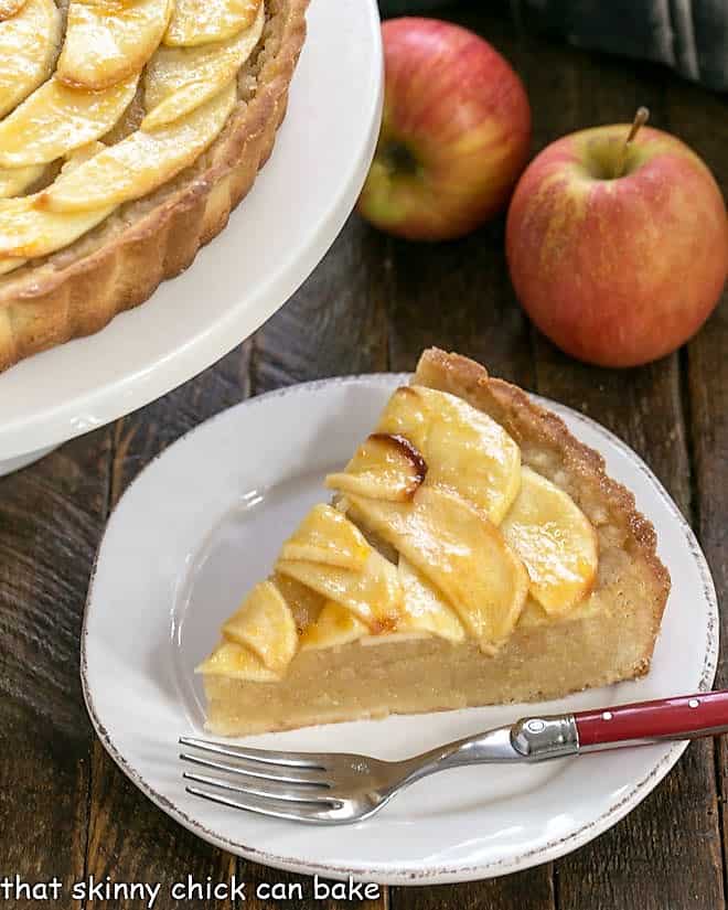 Slice of an apple tart recipe on a round white plate with a red handle fork