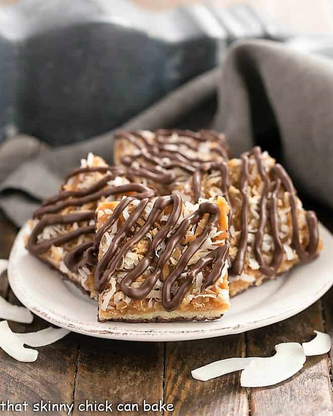 Homemade Samoa Bars - all the same terrific flavors of the classic Girl Scout Cookies with a shortbread base, caramel and coconut topping and chocolate drizzle! Homemade samoa bars on a round plate with shreds of coconut.