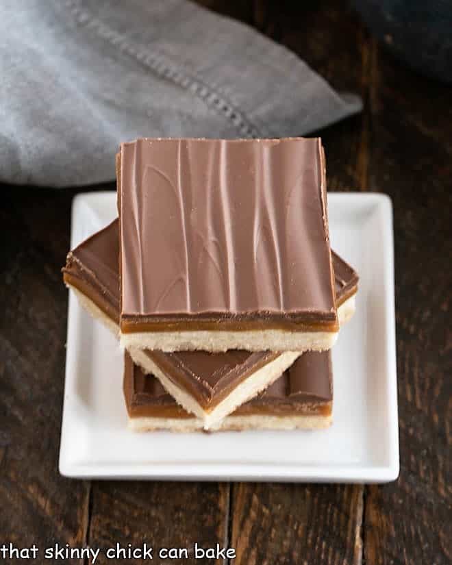 Overhead view of 3 twix bars stacked on a small square white plate.