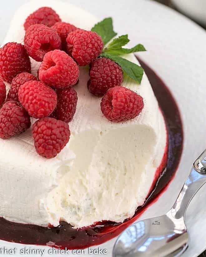 No-Bake cheesecake recipe - an exquisite heart shaped dessert that's perfect for Valentine's Day No-Bake cheesecake recipe topped with fresh raspberries with a scoop removed.