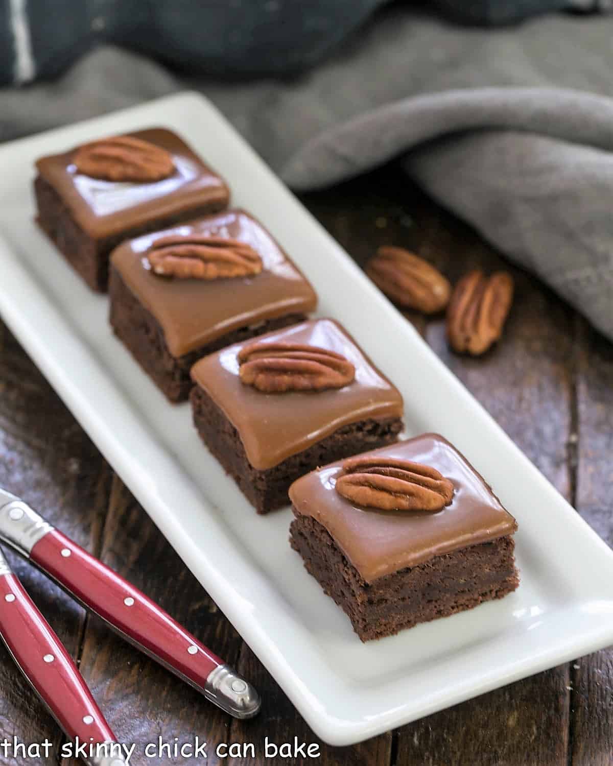 The Ultimate Turtle Brownies - fudgy brownies topped with the perfect chewy caramel and pecan halves A white tray of caramel brownies with 2 red handled forks.
