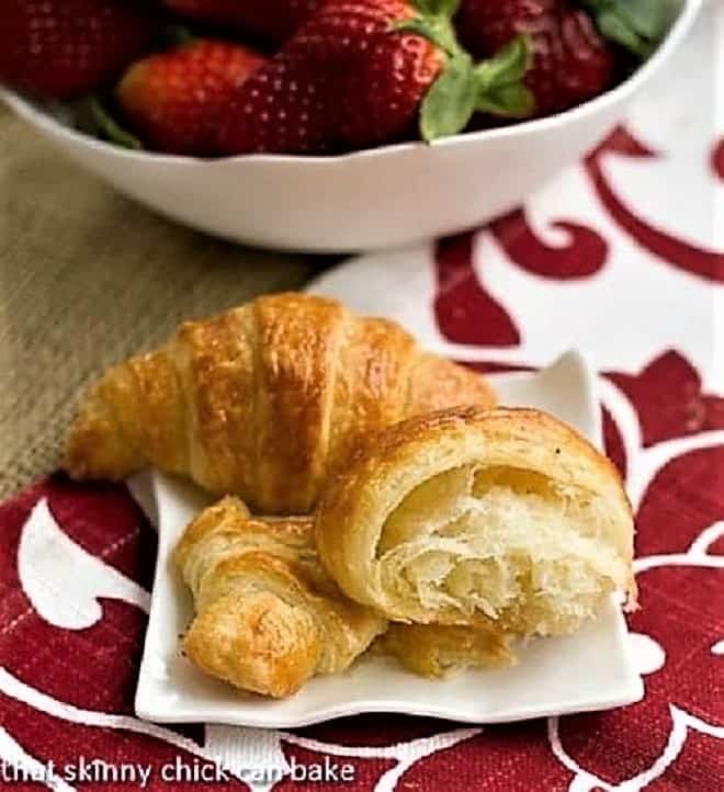 Homemade Classic Croissants - Heavenly, tender, flaky and buttery results! Homemade Classic Croissants on a small white ceramic plate with a bowl of strawberries.