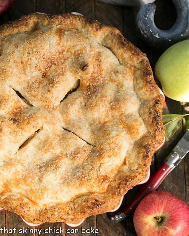 Caramel Apple Pie - a fabulous homemade apple pie enhanced by caramel sauce added to the filling! Overhead view of whole Caramel Apple Pie with apples and a red handle knife.