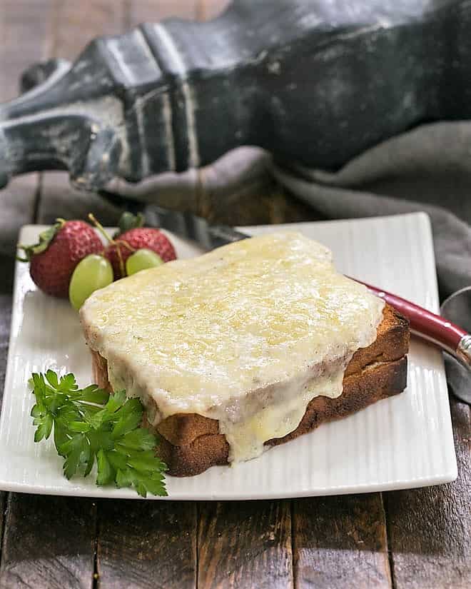 A Croque Monsieur on a white plate with a red handled knife.