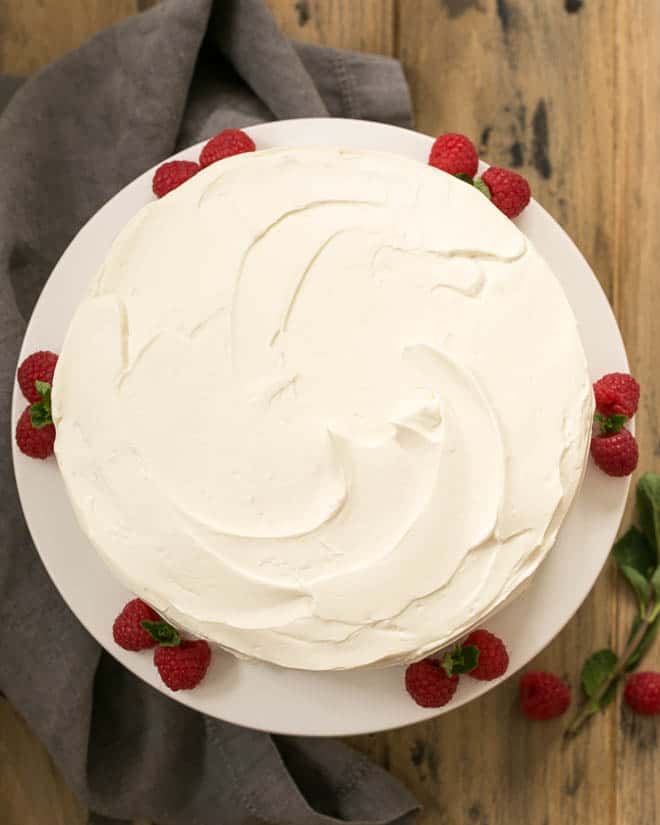 One Layer White Cake Recipe - a dense vanilla cake topped with a luscious white chocolate buttercream Overhead view of vanilla cake on a white cake stand with raspberries and mint.
